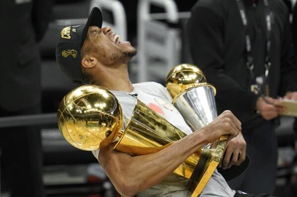 Giannis Antetokounmpo abrazado con el trofeo Larry O'Brien y el trofeo de Finals MVP 2021