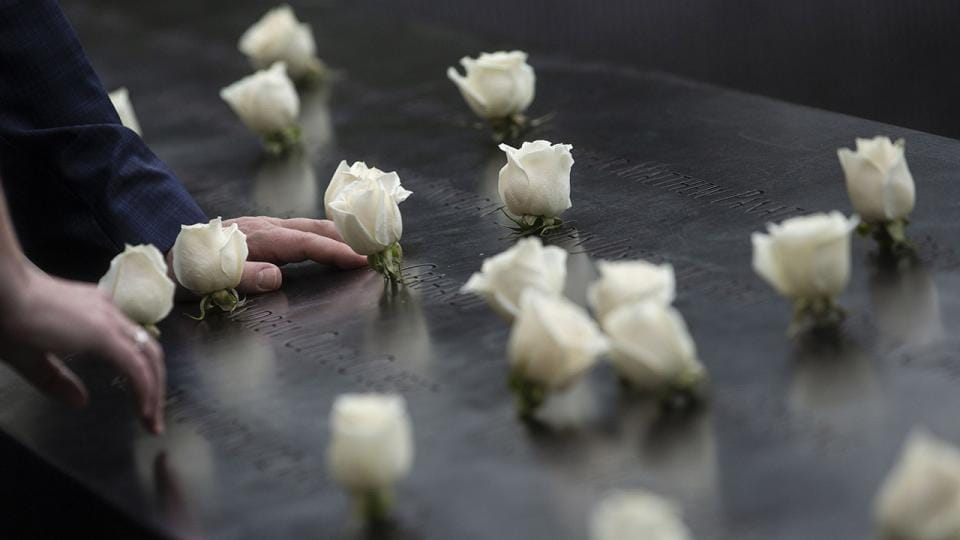 Mano posada sobre un nombre grabado en el Memorial del 11 de Septiembre rodeado de rosas blancas en homenaje a las víctimas