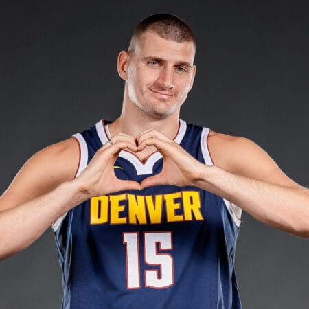 Nikola Jokić forme un cœur avec ses mains en portant le maillot bleu n°15 des Denver Nuggets