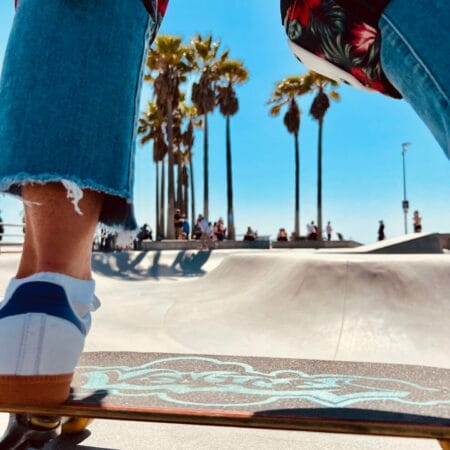 Skateboarder en action au skatepark de Venice Beach avec palmiers en arrière-plan, sous le soleil californien