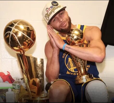 Stephen Curry pose avec le trophée Larry O’Brien et le Finals MVP 2022 dans le vestiaire