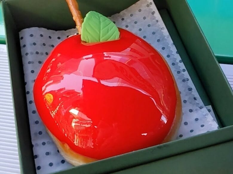 Dónut de Krispy Kreme con forma de manzana roja brillante, presentado en una caja verde, inspirado en Nueva York.