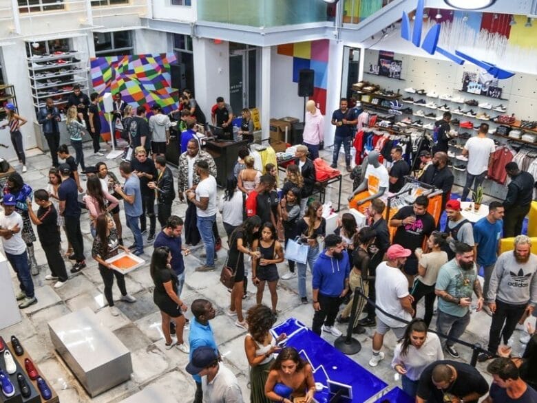 Interior de Shoe Palace Miami con clientes, zapatillas y ropa streetwear.