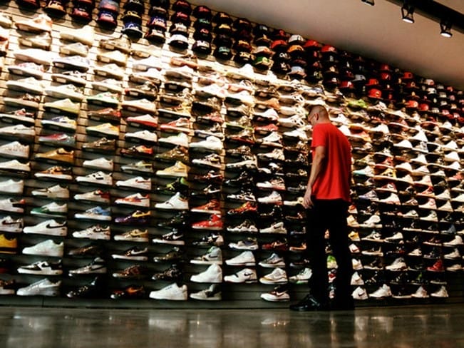 Pared llena de sneakers en Flight Club Los Angeles, con un visitante observando zapatillas exclusivas.