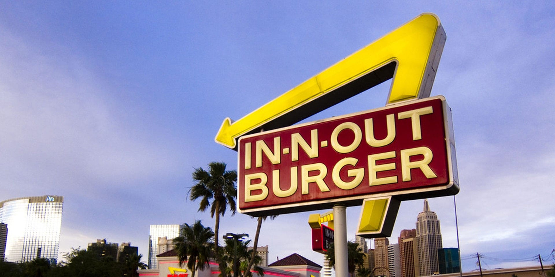 Cartel de In-N-Out Burger con hoteles y palmeras al fondo.