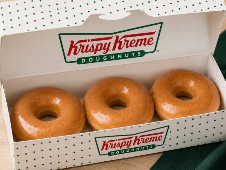 Caja de Krispy Kreme con tres dónuts glaseados clásicos y el logotipo de la marca.