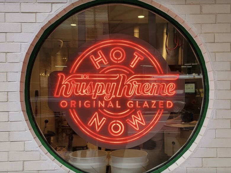 Cartel luminoso Hot Now de Krispy Kreme Original Glazed visto a través de una ventana circular en una tienda de Nueva York.